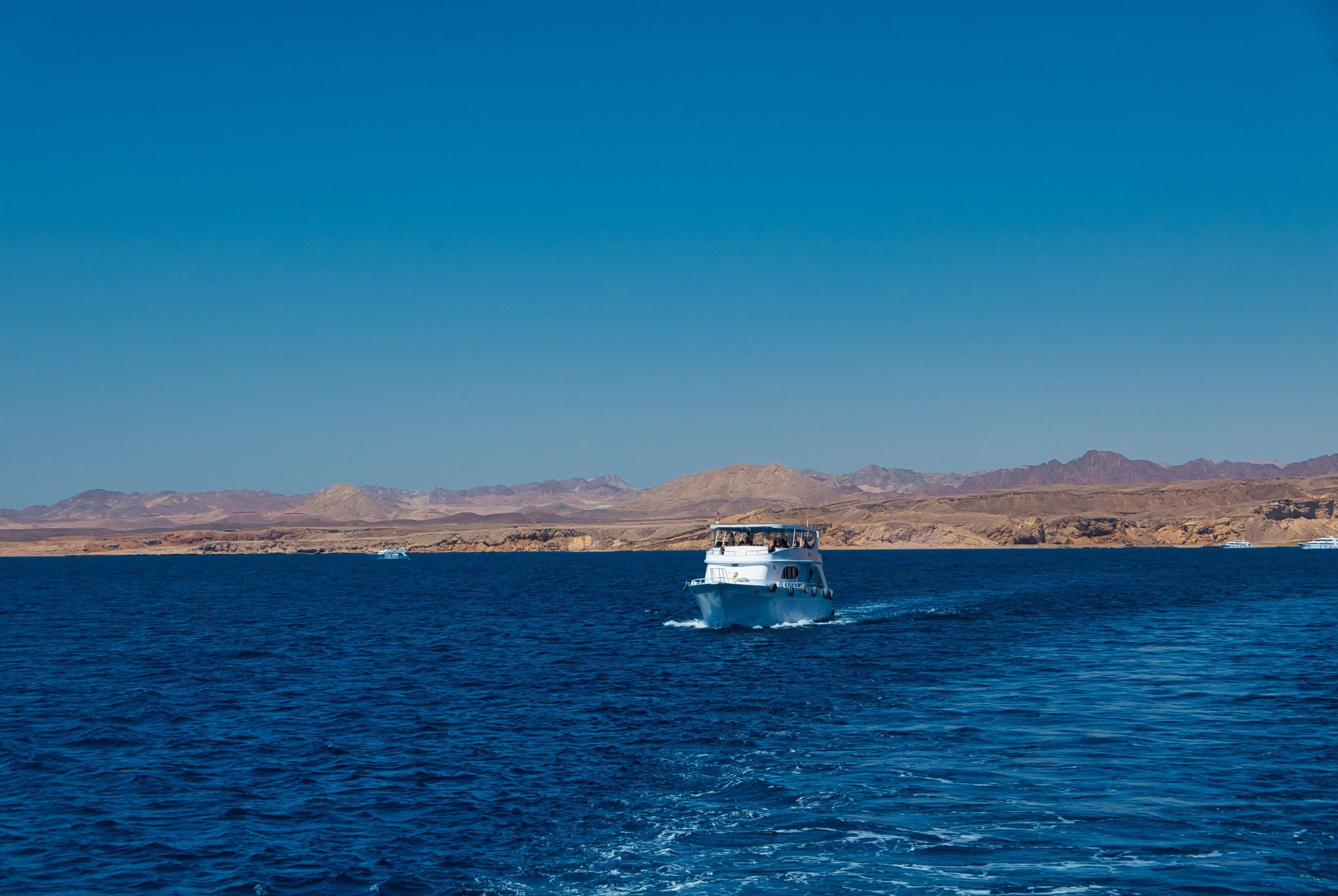 White boat sailing across the Red Sea with mountains in the background.
