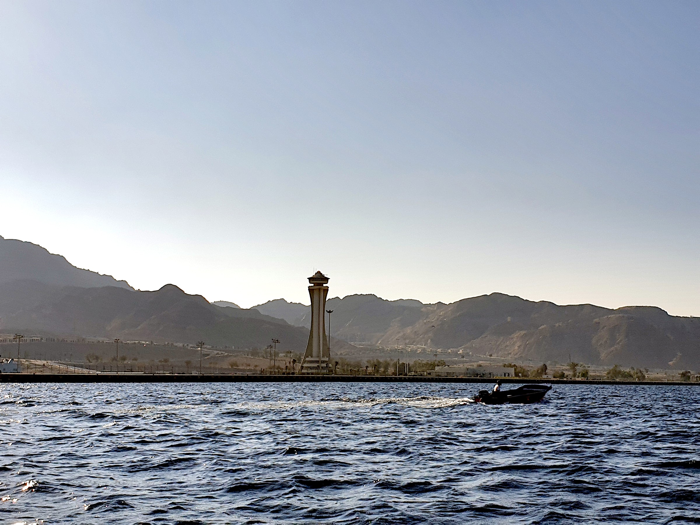 Boat passing the Aqaba waterfront with a tower and mountains in the background.