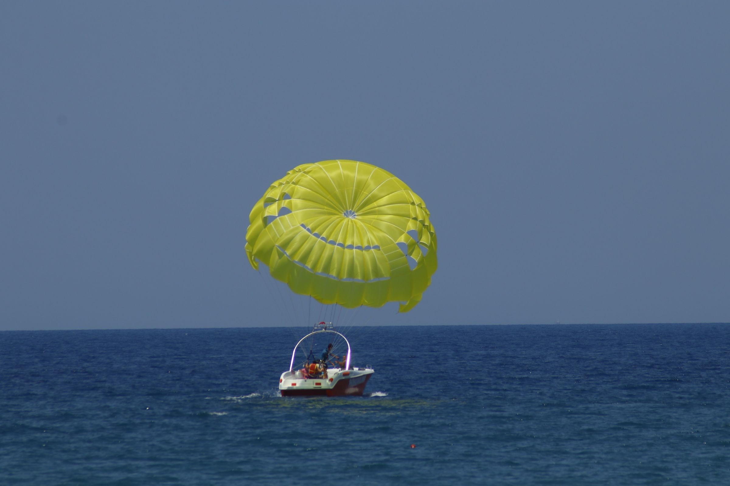 Parasailer flying above the sea while being pulled by a speedboat.