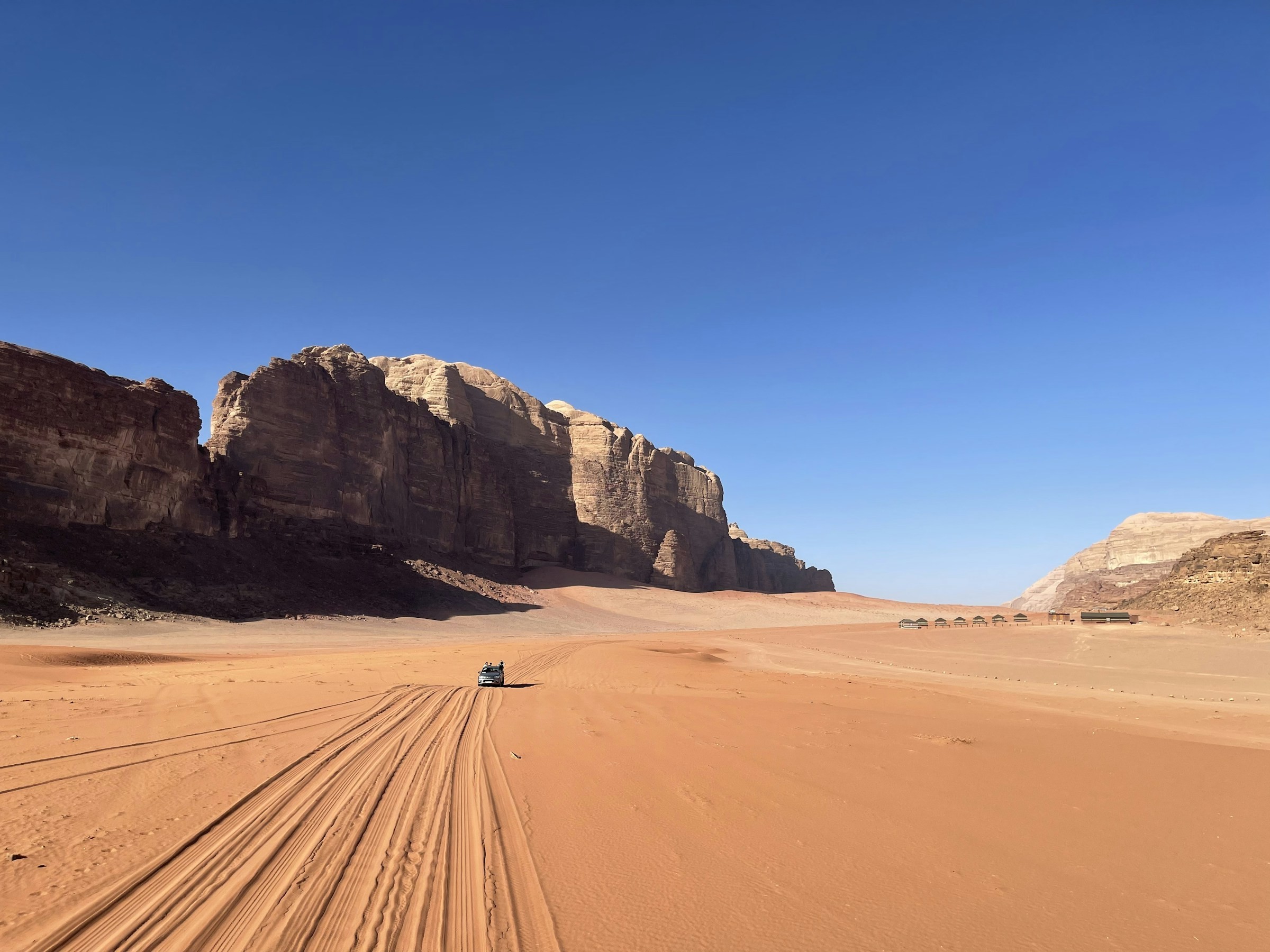Jeep traveling across the Wadi Rum desert beneath sandstone mountains.