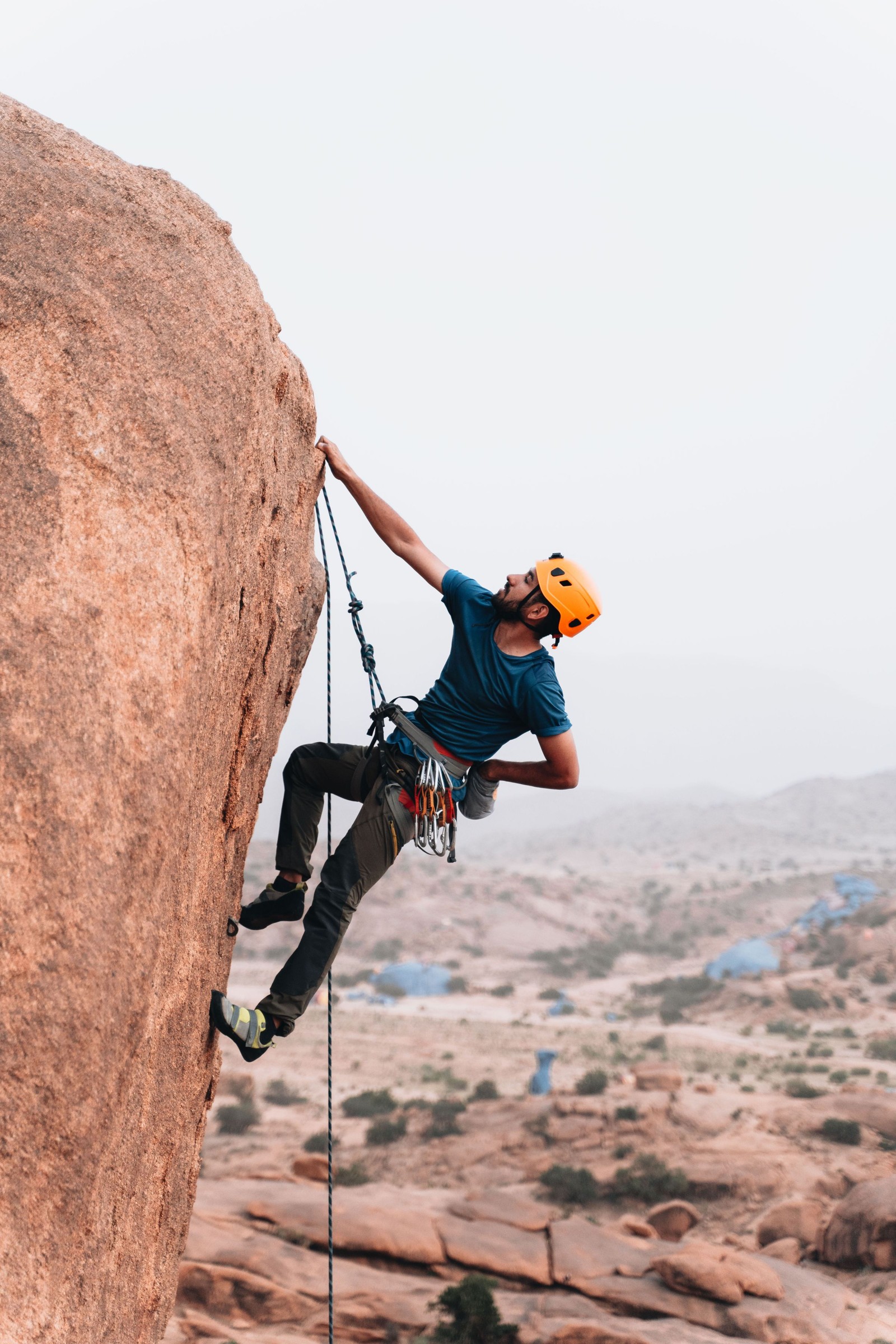 Climber wearing a helmet ascending an outdoor rock face.
