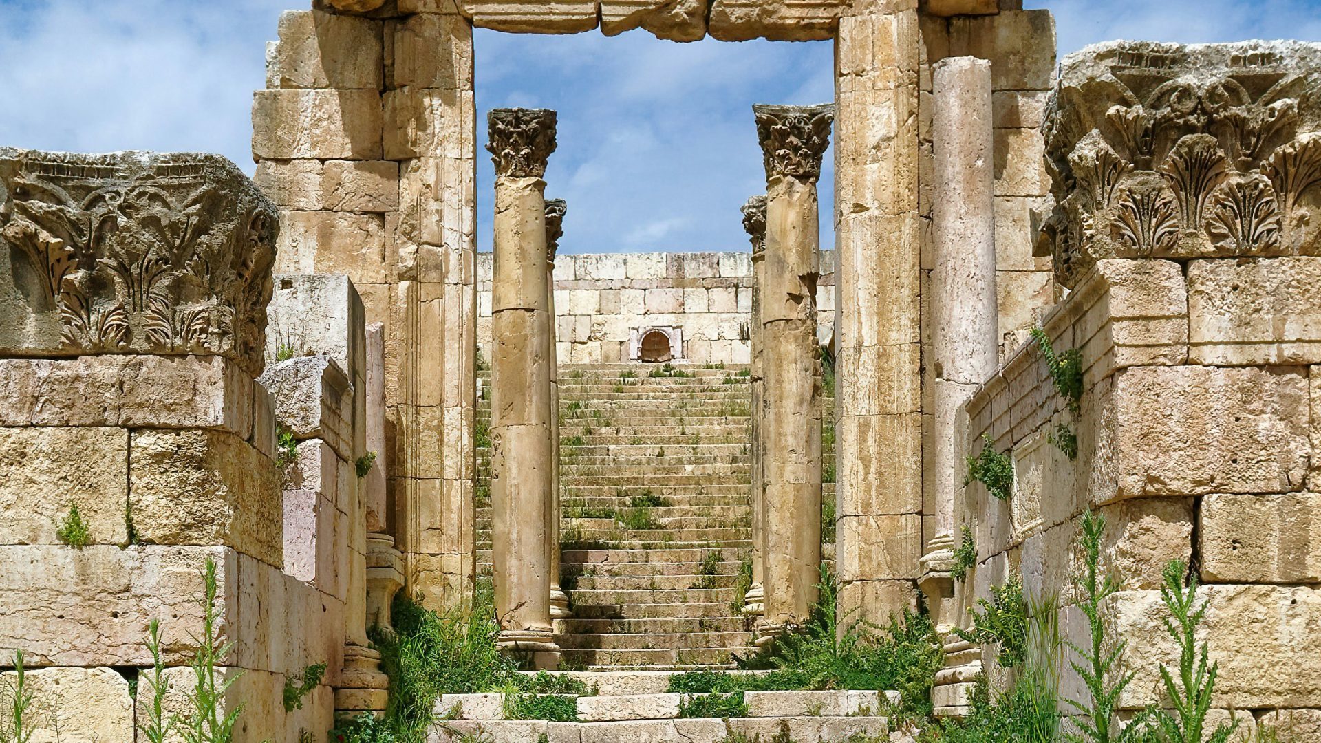 Ancient Roman ruins of Jerash, Jordan, featuring the monumental stone columns and steps of the Temple of Artemis, framed by historic arches under a blue sky
