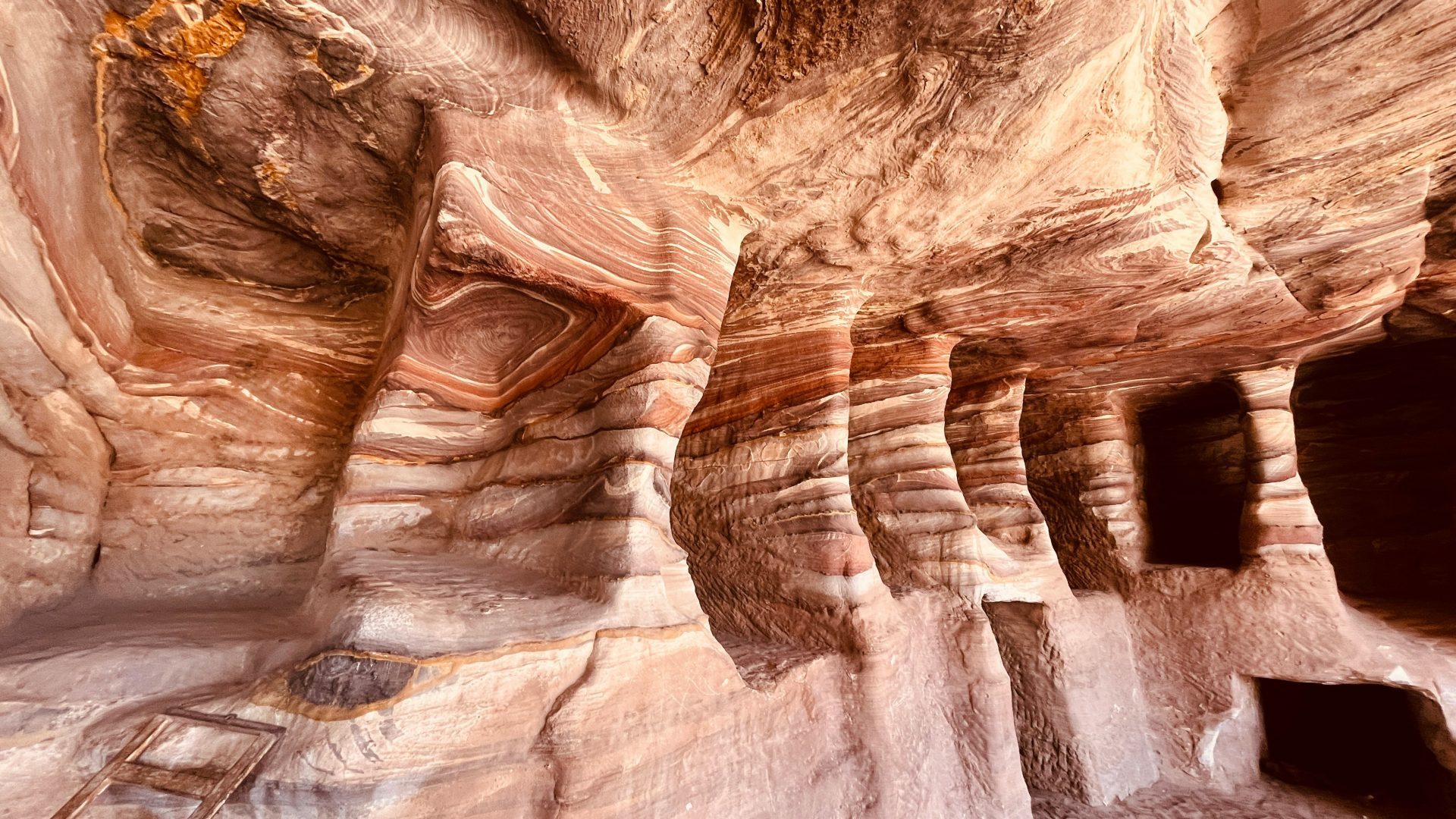 Colorful sandstone rock formations in Petra, Jordan, featuring naturally layered red, pink, white, and orange patterns carved into the ancient canyon walls