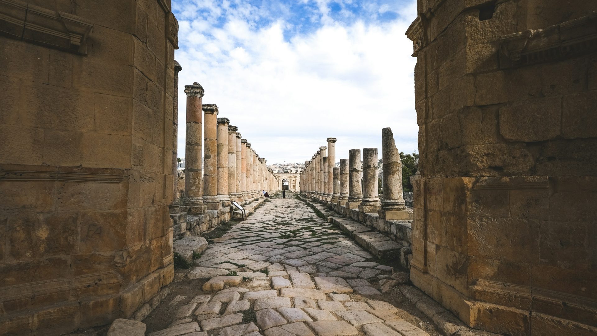 Ancient Roman colonnaded street in Jerash, Jordan, featuring historic stone columns, a preserved cobblestone pathway, and archaeological ruins under a blue sky