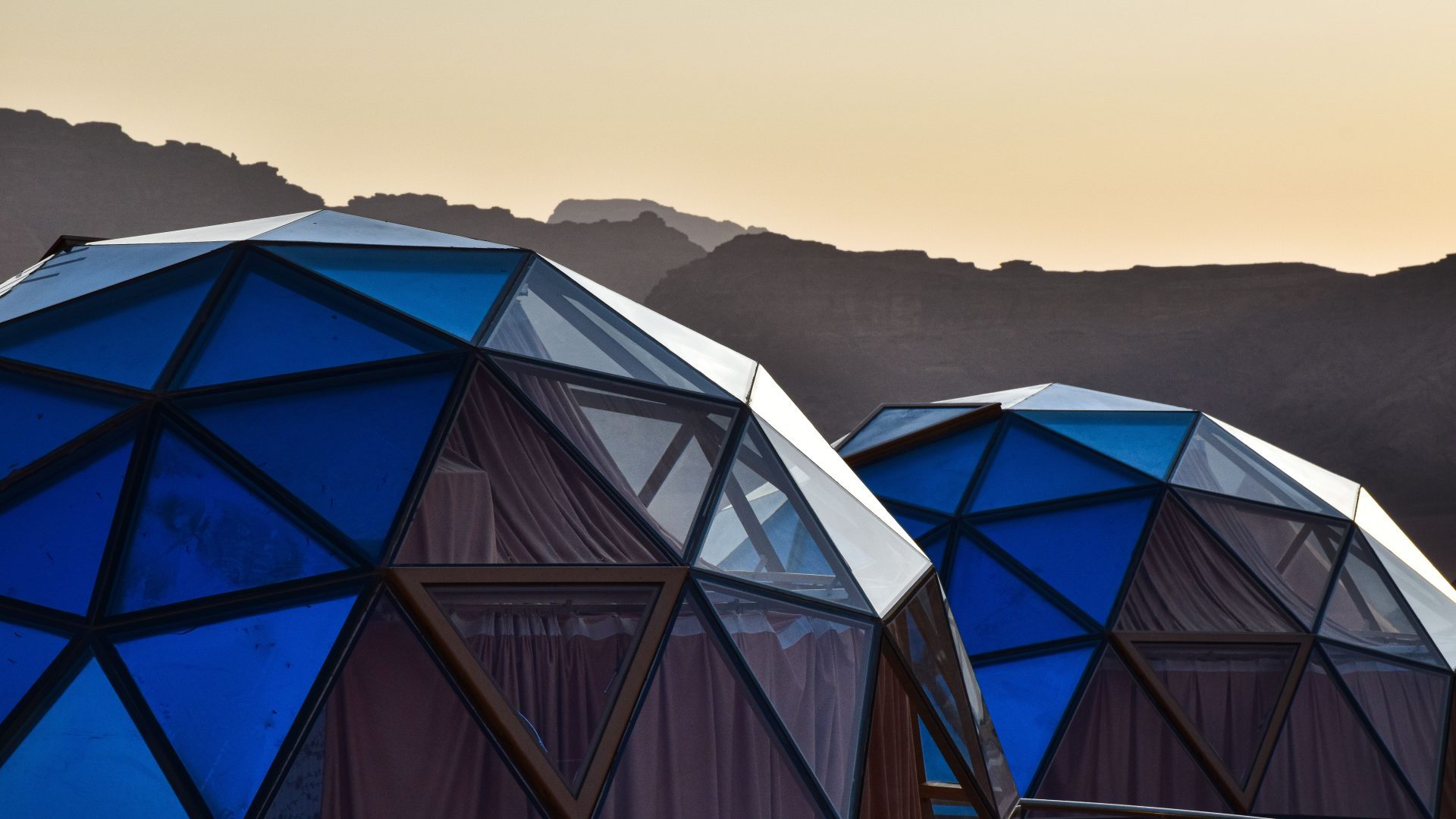 Luxury geodesic dome tents in Wadi Rum, Jordan, featuring modern transparent panoramic windows against dramatic desert mountains at sunset