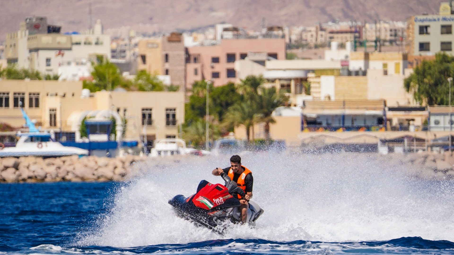 Jet ski adventure on the Red Sea in Aqaba, Jordan, rider speeding across the blue water with the Aqaba coastline and city in the background