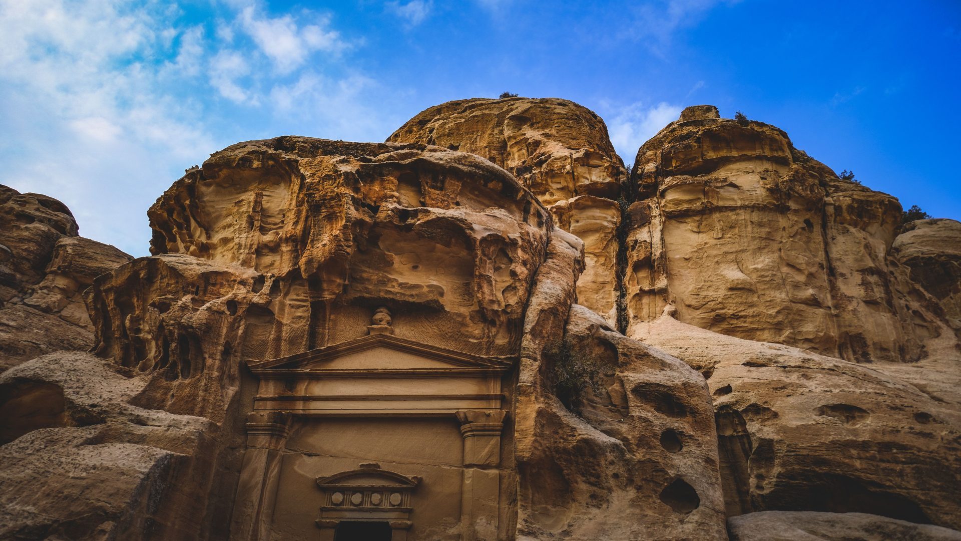Ancient Nabataean rock-cut tomb carved into the sandstone cliffs of Petra, Jordan, under a vivid blue sky