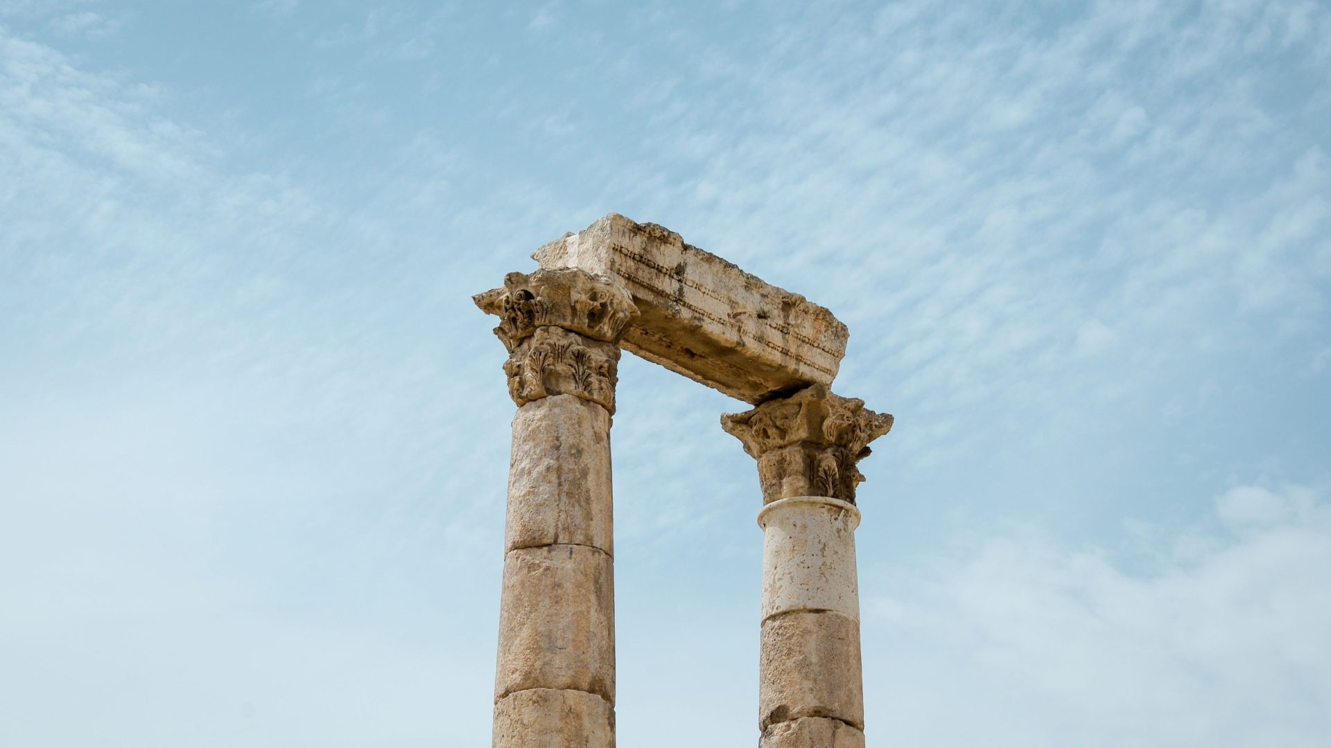 Ancient Roman columns in Jerash, Jordan, featuring weathered Corinthian capitals and historic stone architecture against a clear blue sky