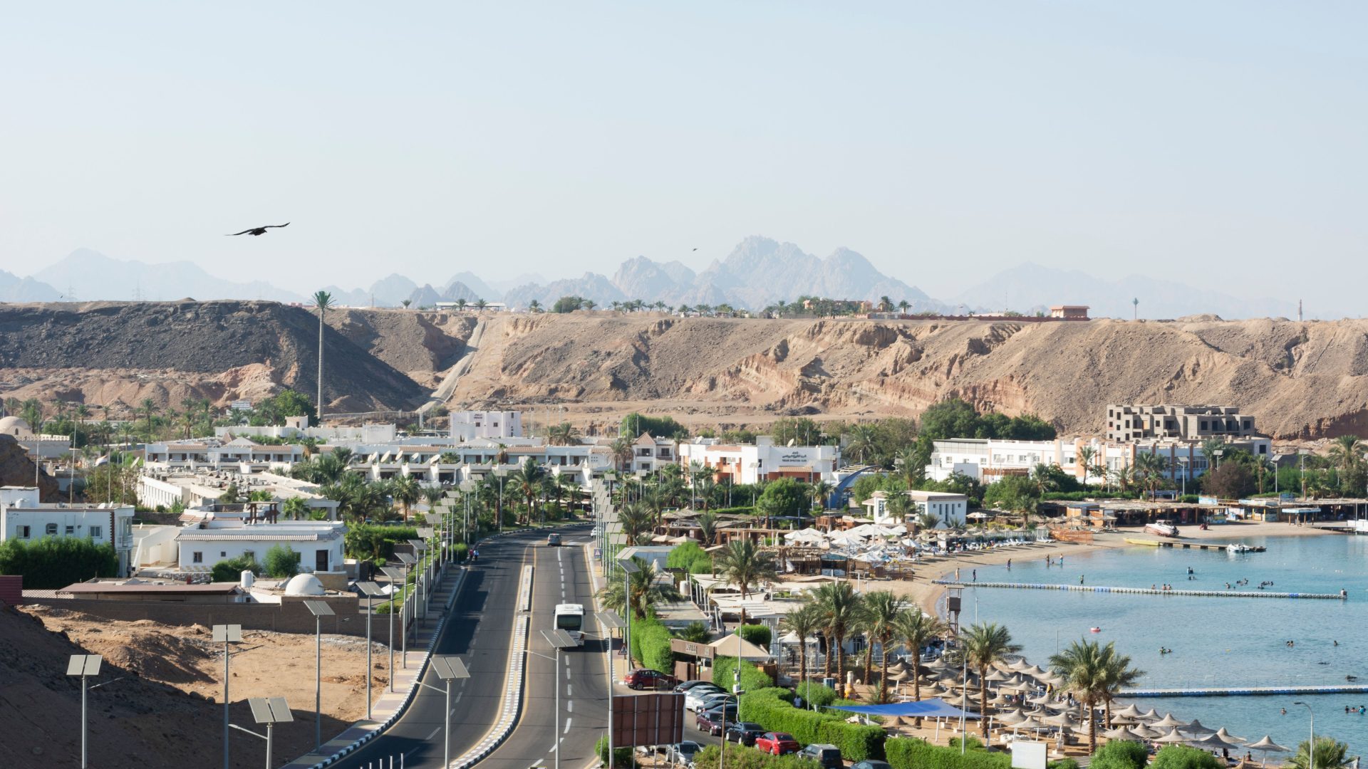 Aqaba city and Red Sea coastline in Jordan, featuring a scenic coastal road, resorts, palm trees, blue waters, and desert mountains in the background