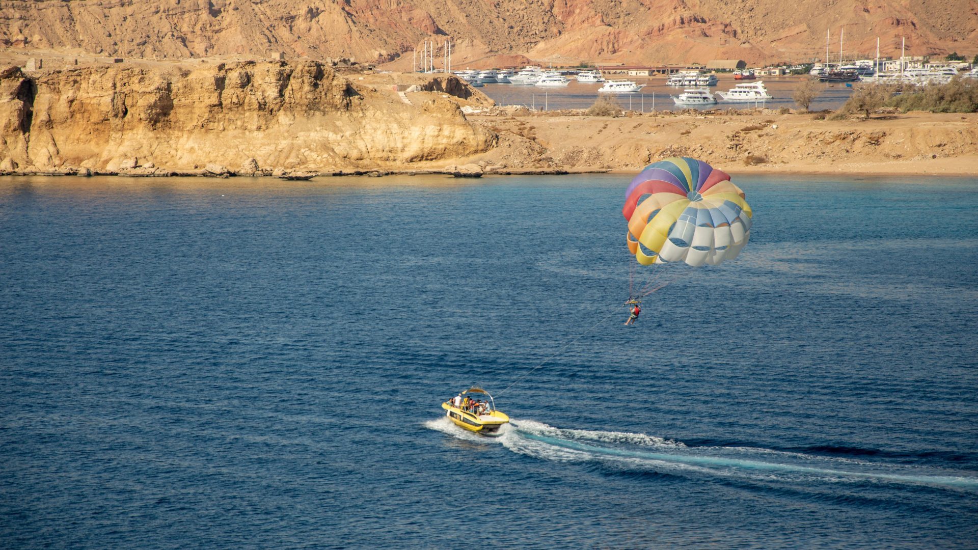 Parasailing adventure over the Red Sea in Aqaba, Jordan, with a speedboat towing a colorful parachute along the scenic coastline