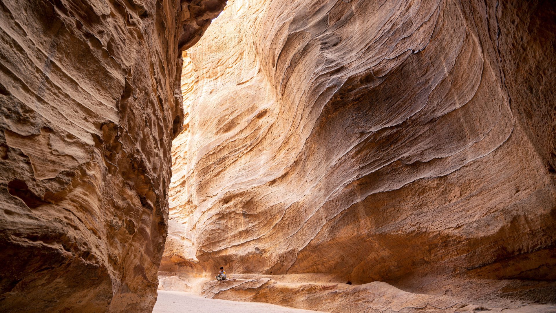 The Siq in Petra, Jordan, a narrow sandstone canyon with towering rose-red rock walls and visitors walking through the ancient passage toward Petra