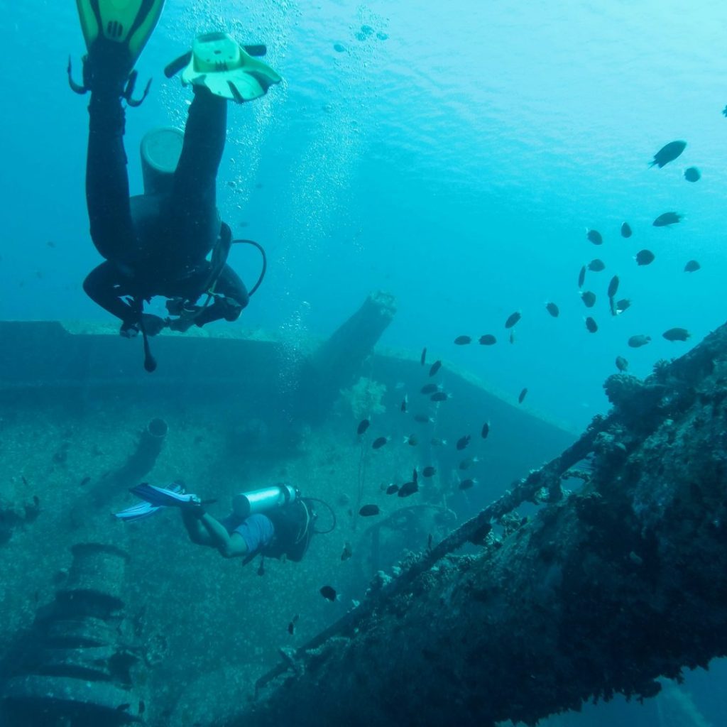 Scuba diving in the Red Sea in Aqaba, Jordan, with divers exploring an underwater shipwreck surrounded by tropical fish and clear blue water