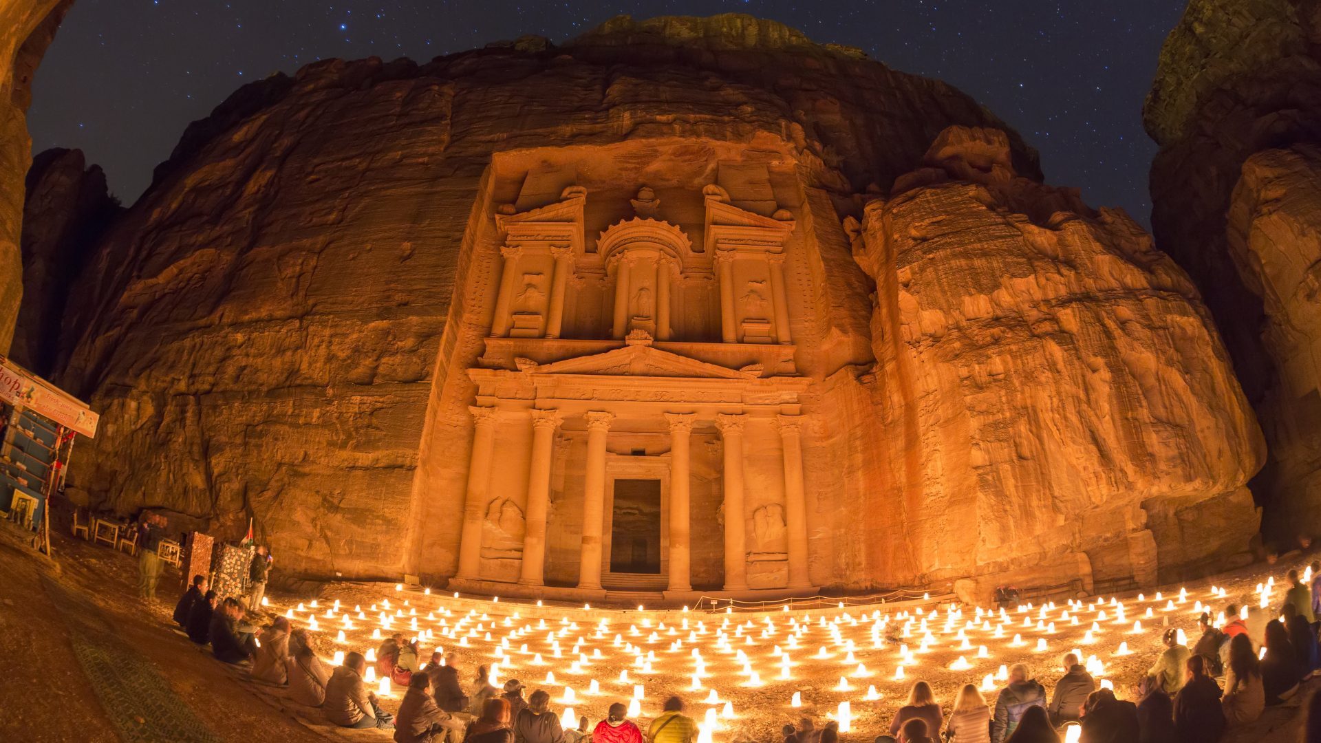 Petra by Night in Jordan, Al-Khazneh (The Treasury) illuminated by hundreds of glowing candles, surrounded by dramatic rose-red sandstone cliffs
